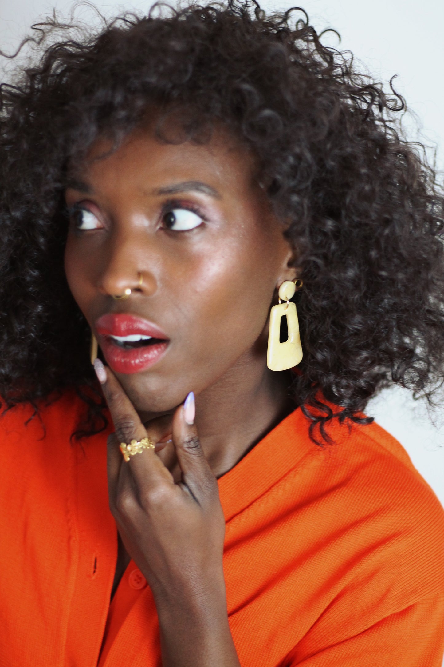Gorgeous young woman wearing the Audrey earrings in a glossy golden color by the brand Dress To Finesse. This brand is created by Anna De Ceulaer in Antwerp, Belgium. The Audrey earrings are made of clay and are very lightweight. She is also wearing the Madeline ring in gold which features flowers of different sizes.