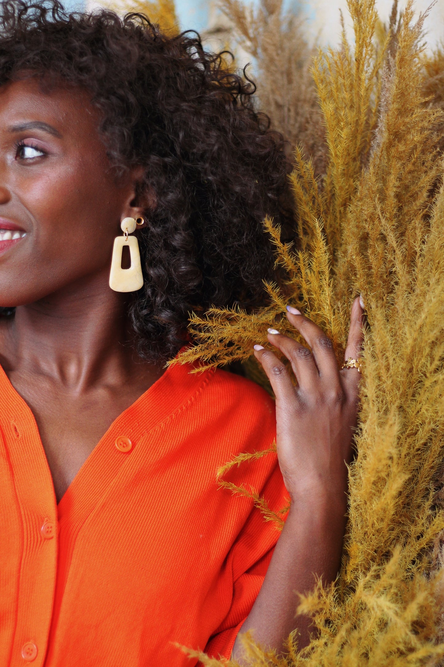 Gorgeous young woman wearing the Audrey earrings in a glossy golden color by the brand Dress To Finesse. This brand is created by Anna De Ceulaer in Antwerp, Belgium. The Audrey earrings are made of clay and are very lightweight. She is also wearing the Madeline ring in gold which features flowers of different sizes.