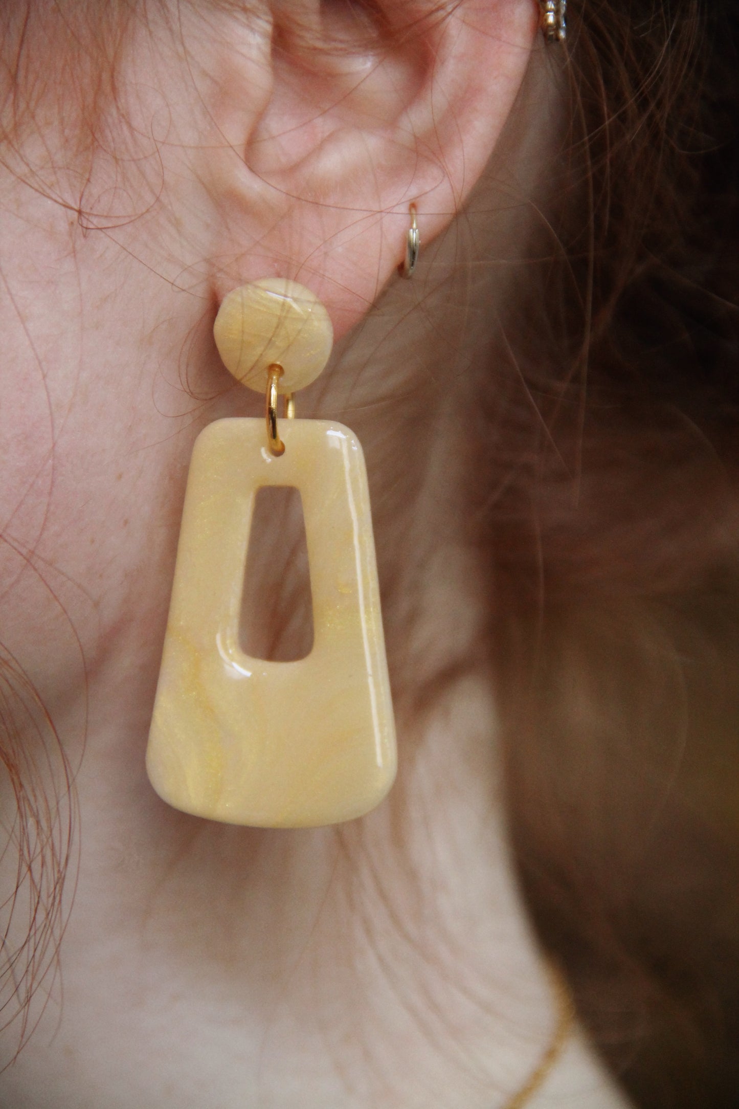A close up photo of the Audrey earrings in a glossy golden color by the brand Dress To Finesse. This brand is created by Anna De Ceulaer in Antwerp, Belgium. The Audrey earrings are made of clay and are very lightweight.