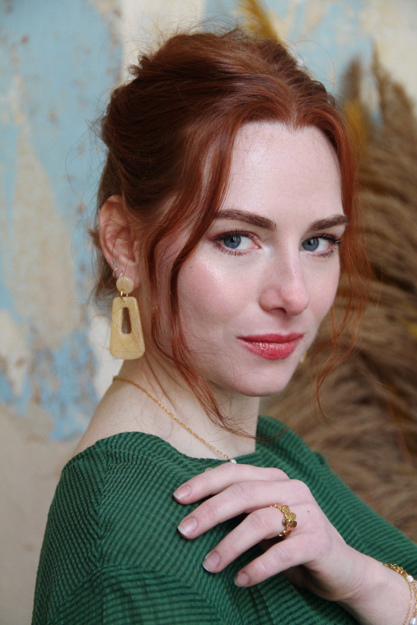 Gorgeous young woman wearing the Audrey earrings in a glossy golden color by the brand Dress To Finesse. This brand is created by Anna De Ceulaer in Antwerp, Belgium. The Audrey earrings are made of clay and are very lightweight. The model is also wearing the Fae necklace which features genuine freshwater pearls. She is also wearing the Madeline ring in gold which features flowers of different sizes.