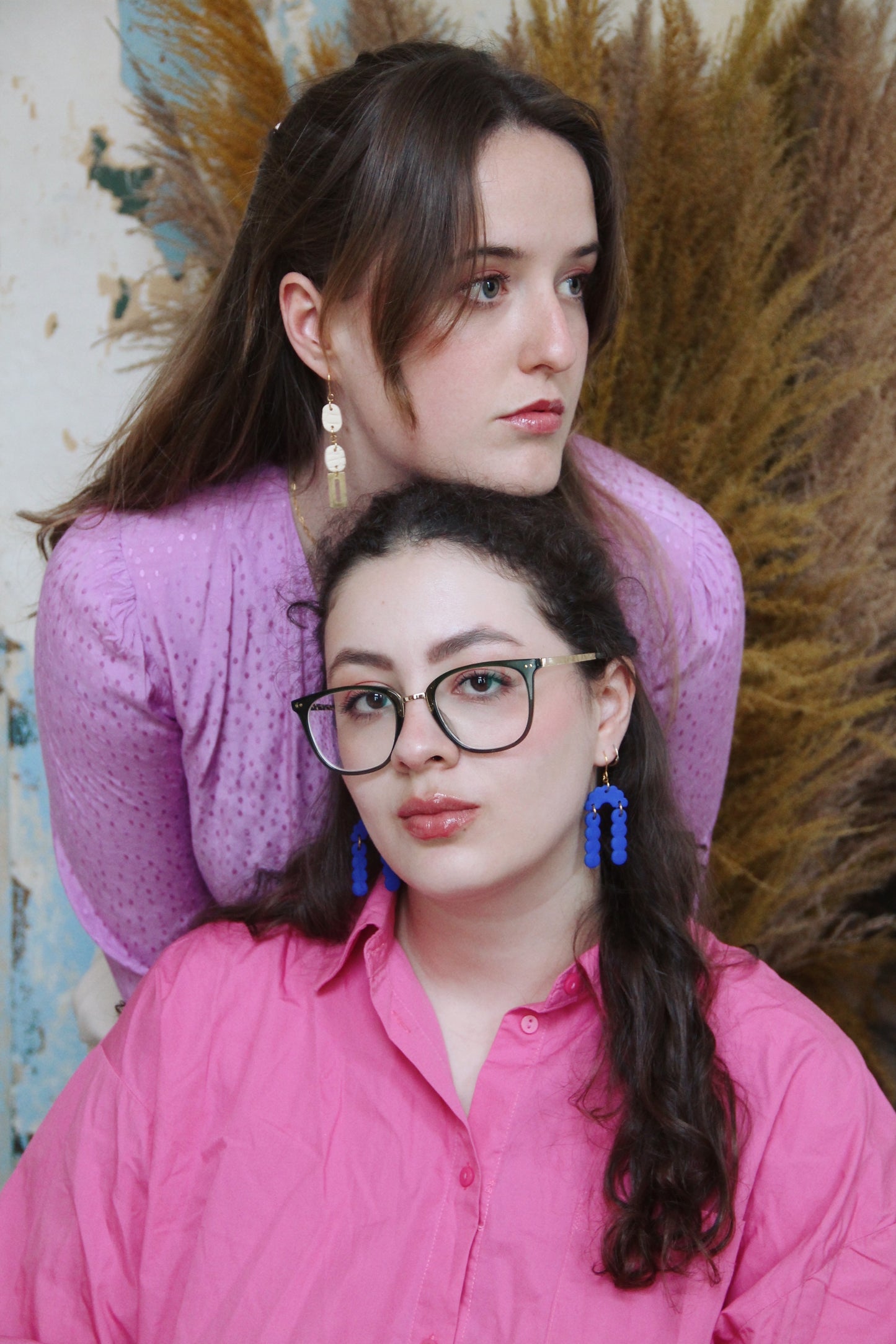 Gorgeous young woman wearing the Beth earrings in beige with a radiant brass element by the brand Dress To Finesse. The other girl on the right is wearing the Elisabeth earrings in royal blue. This brand is created by Anna De Ceulaer in Antwerp, Belgium. The Beth earrings are made of clay and are very lightweight.