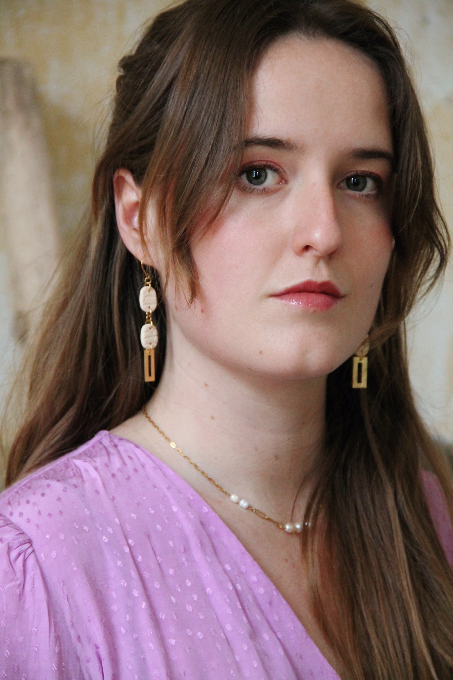 Gorgeous young woman wearing the Beth earrings in beige with a radiant brass element by the brand Dress To Finesse. This brand is created by Anna De Ceulaer in Antwerp, Belgium. The Beth earrings are made of clay and are very lightweight.