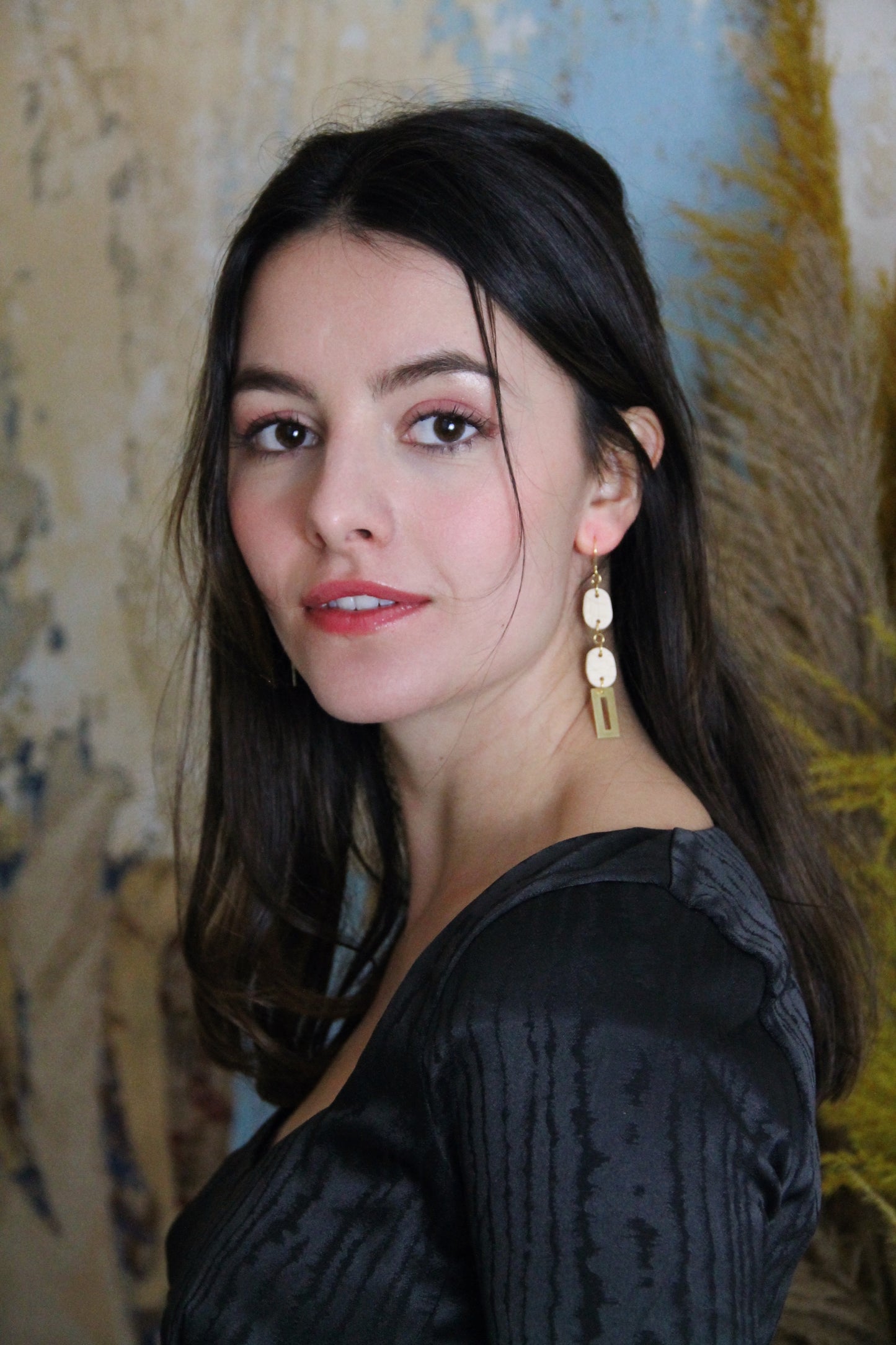 Gorgeous young woman wearing the Beth earrings in beige with a radiant brass element by the brand Dress To Finesse. This brand is created by Anna De Ceulaer in Antwerp, Belgium. The Beth earrings are made of clay and are very lightweight.