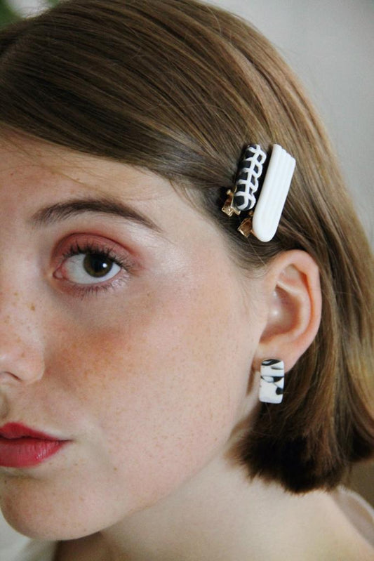 Model wears minimalist earrings in black and white marble print. She also wears handmade hair pins in the shape of a bow.