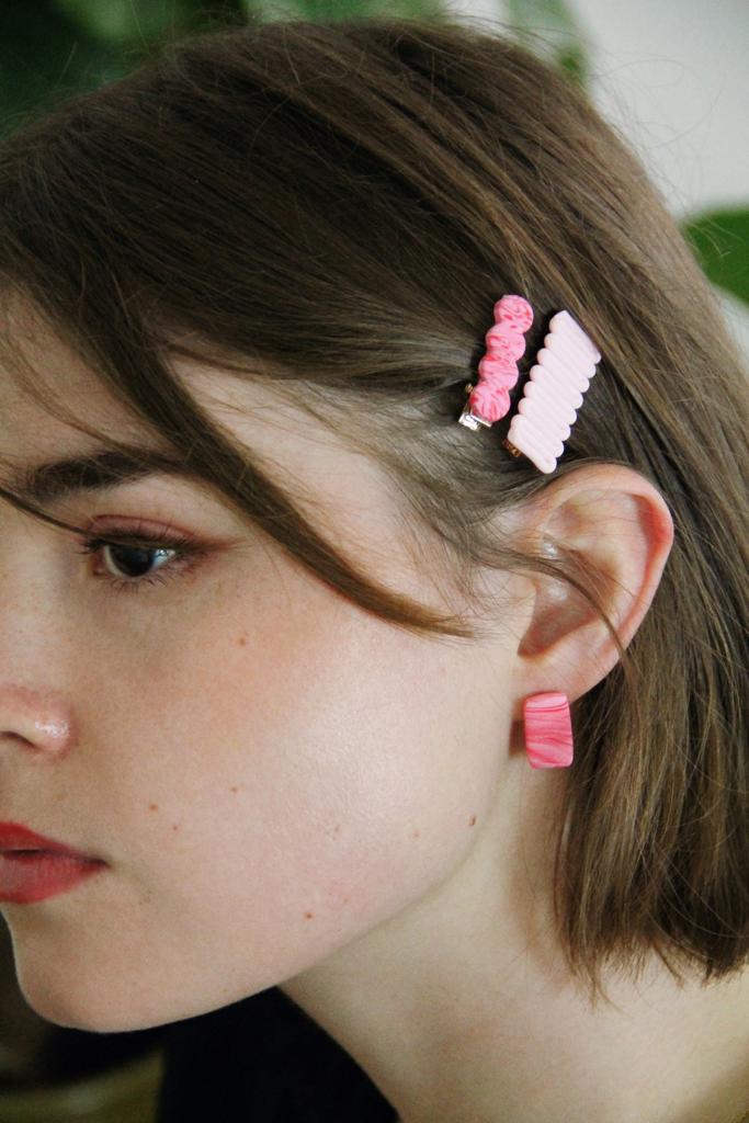 Model wears minimalist earrings in pink and red marble print. She also wears handmade hair pins in the shape of a bow.