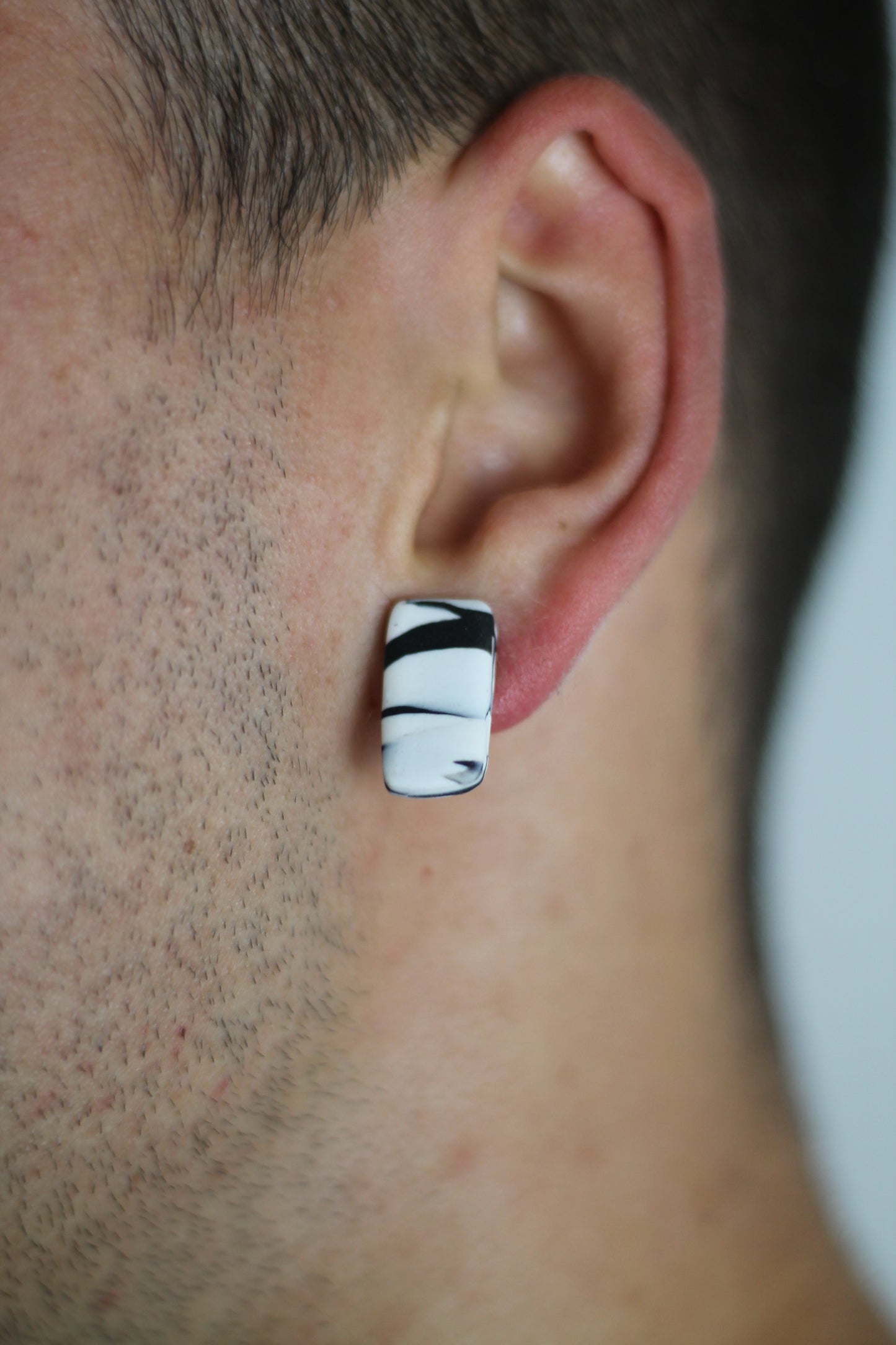 Model wears minimalist earrings in black and white marble print. He also wears handmade hair pins in the shape of a bow.