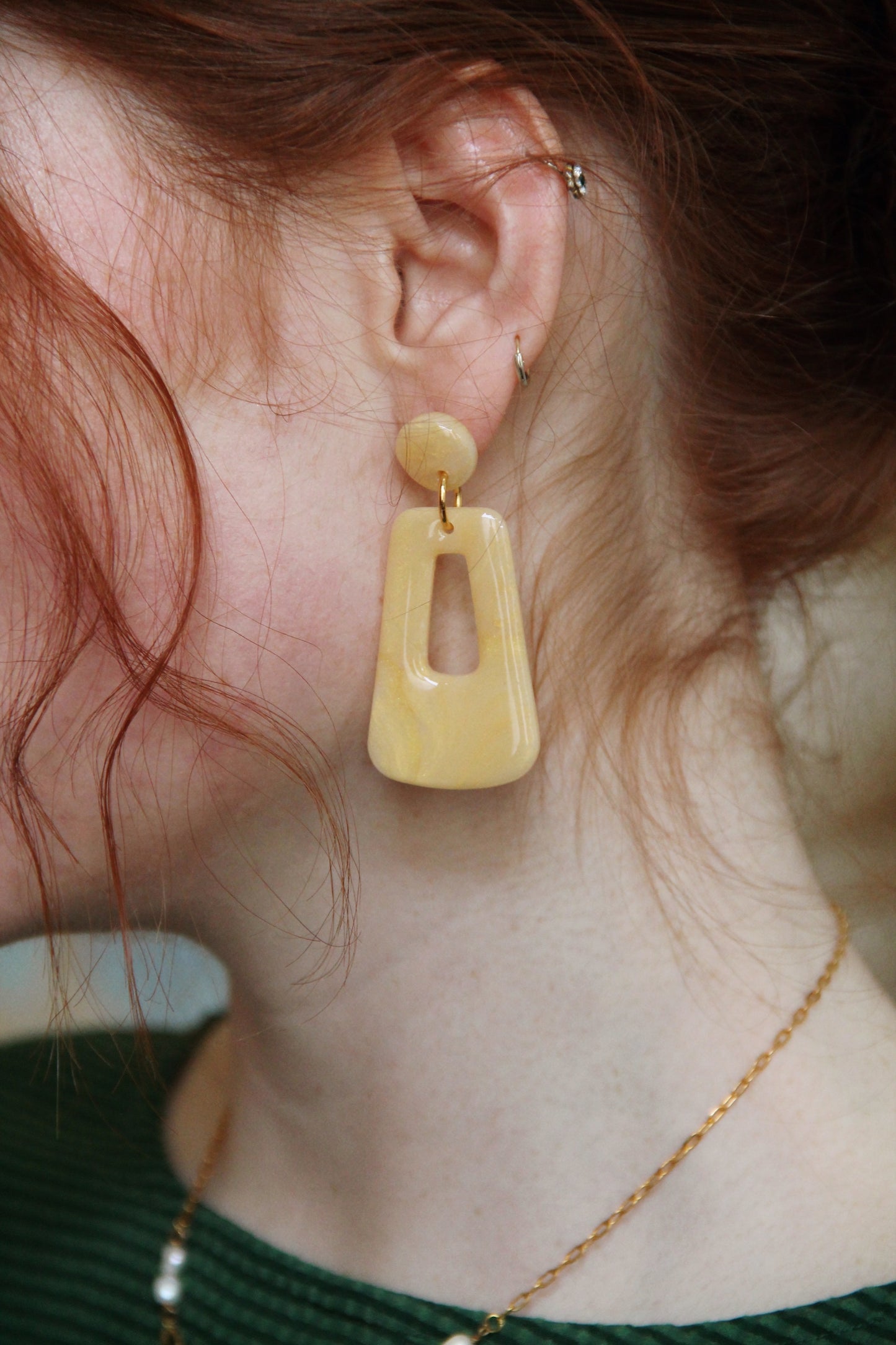 A close up photo of the Audrey earrings in a glossy golden color by the brand Dress To Finesse. This brand is created by Anna De Ceulaer in Antwerp, Belgium. The Audrey earrings are made of clay and are very lightweight.