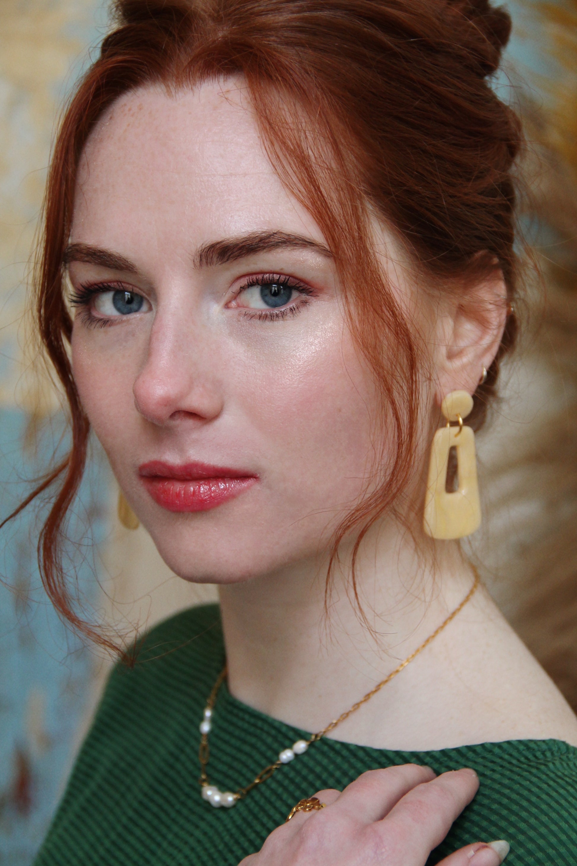 Gorgeous young woman wearing the Audrey earrings in a glossy golden color by the brand Dress To Finesse. This brand is created by Anna De Ceulaer in Antwerp, Belgium. The Audrey earrings are made of clay and are very lightweight. The model is also wearing the Fae necklace which features genuine freshwater pearls.