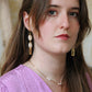 Gorgeous young woman wearing the Beth earrings in beige with a radiant brass element by the brand Dress To Finesse. This brand is created by Anna De Ceulaer in Antwerp, Belgium. The Beth earrings are made of clay and are very lightweight.