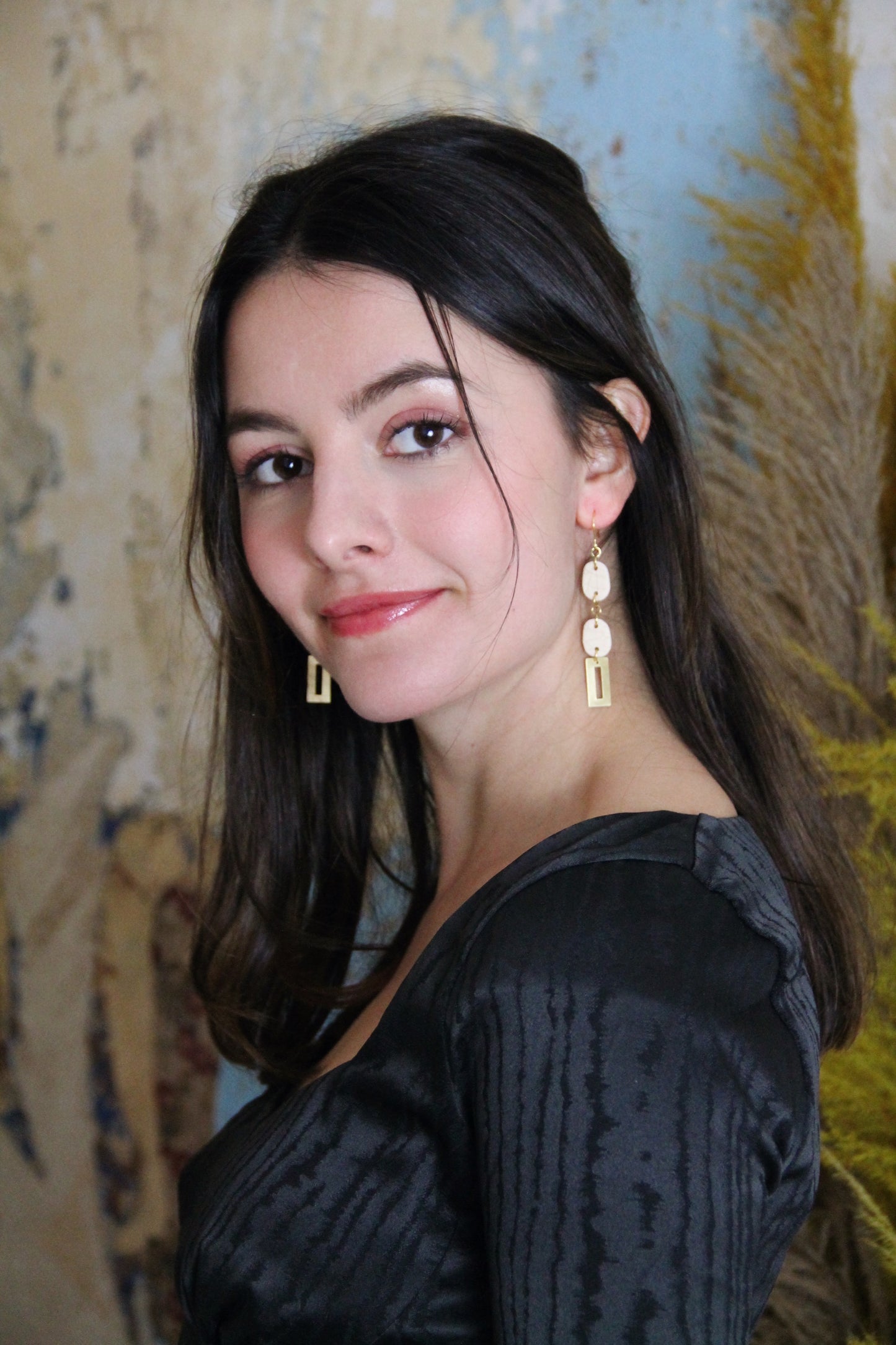 Gorgeous young woman wearing the Beth earrings in beige with a radiant brass element by the brand Dress To Finesse. This brand is created by Anna De Ceulaer in Antwerp, Belgium. The Beth earrings are made of clay and are very lightweight.