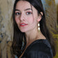 Gorgeous young woman wearing the Beth earrings in beige with a radiant brass element by the brand Dress To Finesse. This brand is created by Anna De Ceulaer in Antwerp, Belgium. The Beth earrings are made of clay and are very lightweight.